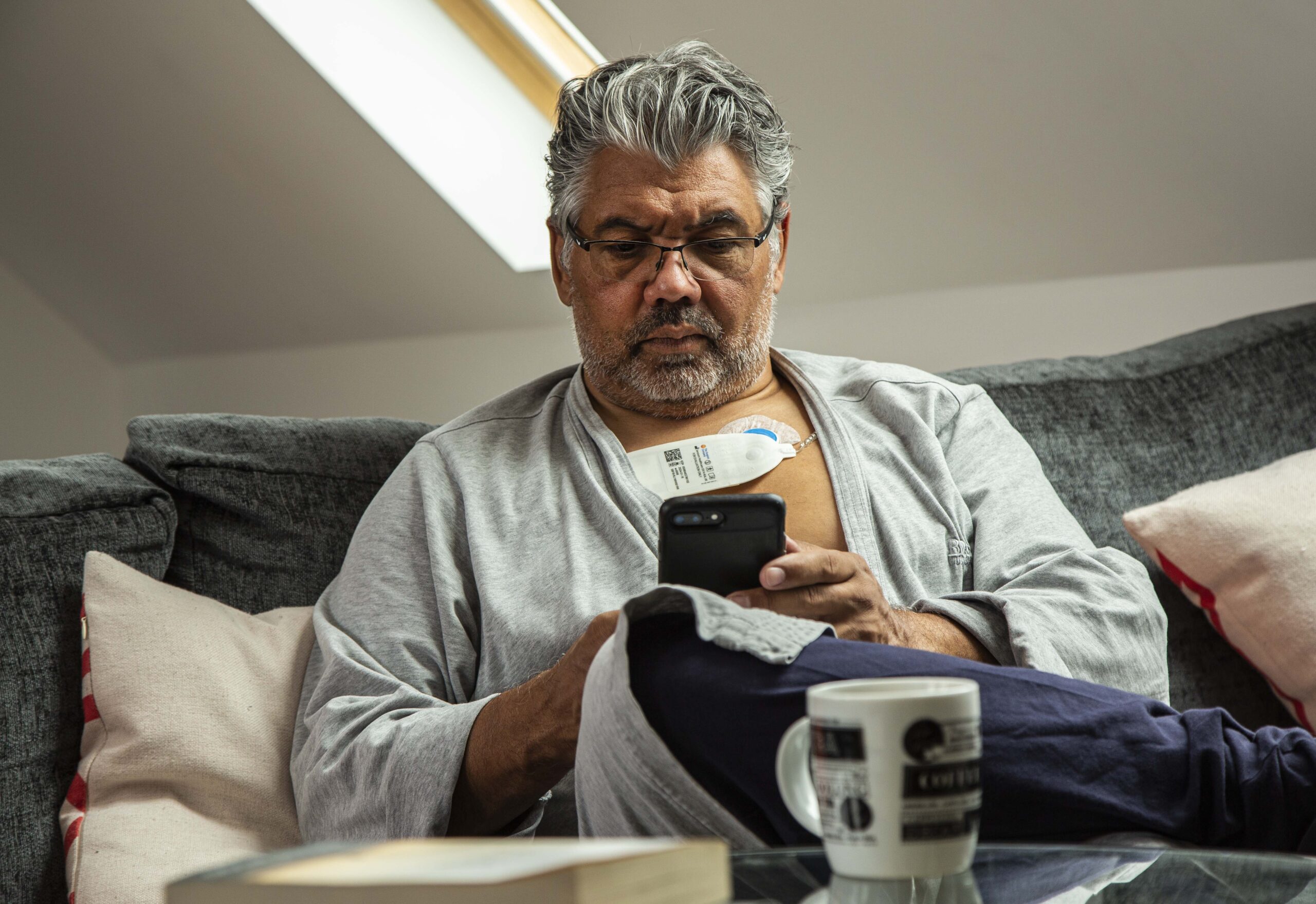 Middle aged male with Sensium wireless vitals patch at home, on the couch on his phone